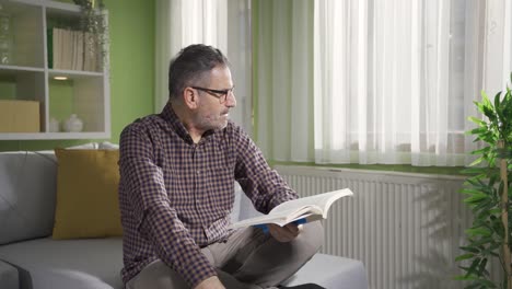 Bearded-man-with-glasses-is-reading-a-book-by-the-window.